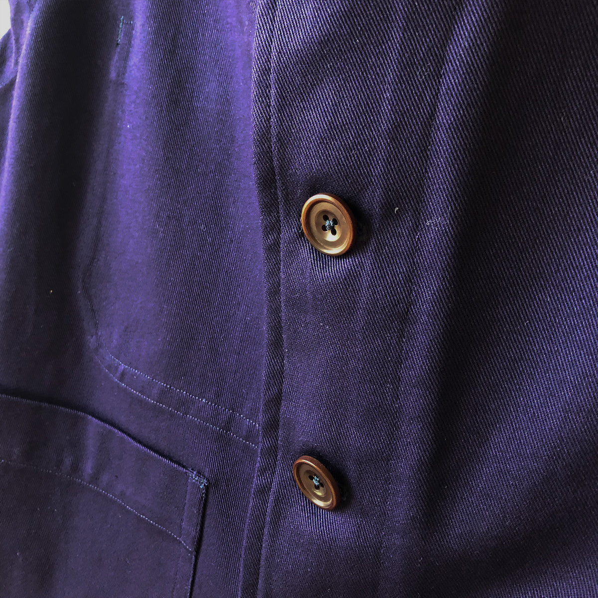 Close-up of a dark purple woven fabric garment with two bronze-colored buttons on the front.