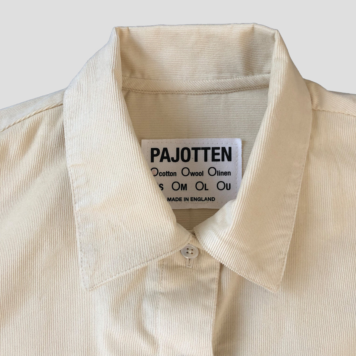 Close-up of a cream-colored corduroy shirt collar with a visible white brand label reading 'PAJOTTEN'.