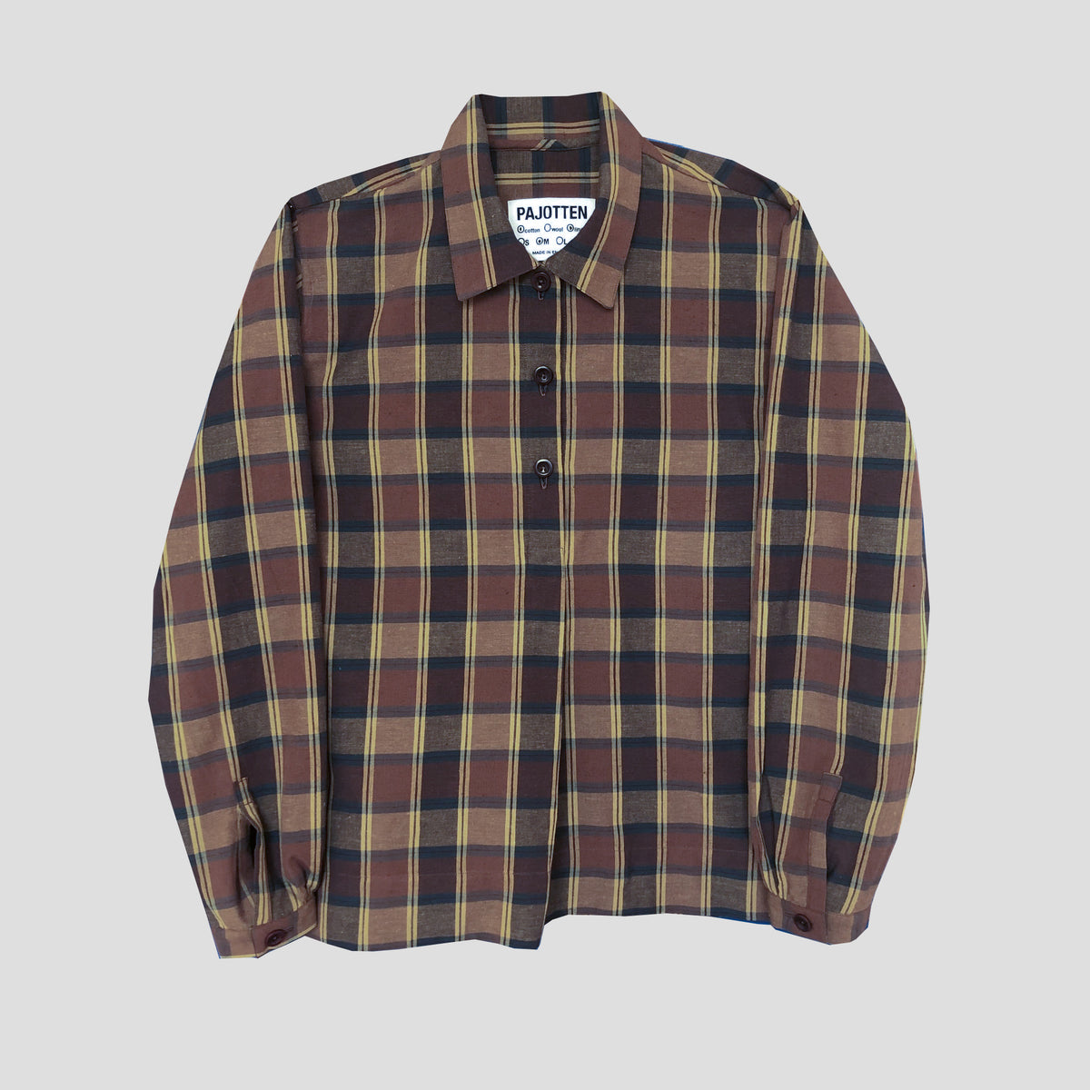 A long-sleeve button-up plaid shirt by Pakotten, featuring a brown, beige, and navy tartan pattern, displayed flat against a light gray background.