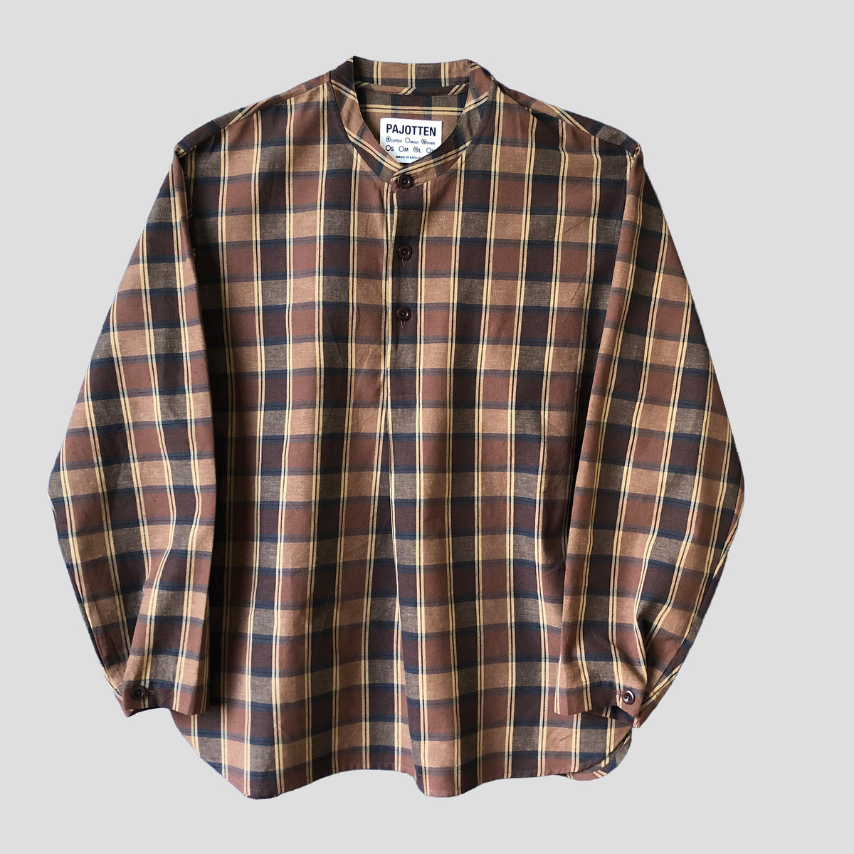 A long-sleeve plaid button-up shirt by Pajotten, featuring a brown, beige, and black checkered pattern with a mandarin collar, laid flat against a light gray background.