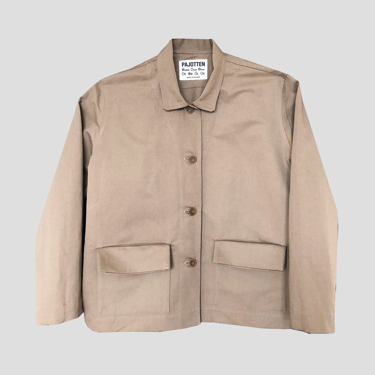 A light beige canvas utility jacket with a collar, four front buttons, and two large front flap pockets, laid flat on a light gray background. The brand label inside the collar reads 'PAJOTTEN'.
