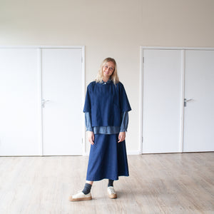 smiling blond woman standing in a sunlit room wearing an indigo denim overtop and skirt facing forward