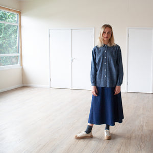 smiling blonde young woman standing in a sunlit room wearing a blue cotton hemp shirt
