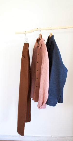 Simple menswear outfit hanging from a sloping wooden rail against a white background shop pajotten menswear sustainable made in the uk 