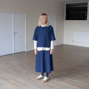 smiling blond woman standing in a sunlit room wearing an indigo denim overtop and skirt facing forward