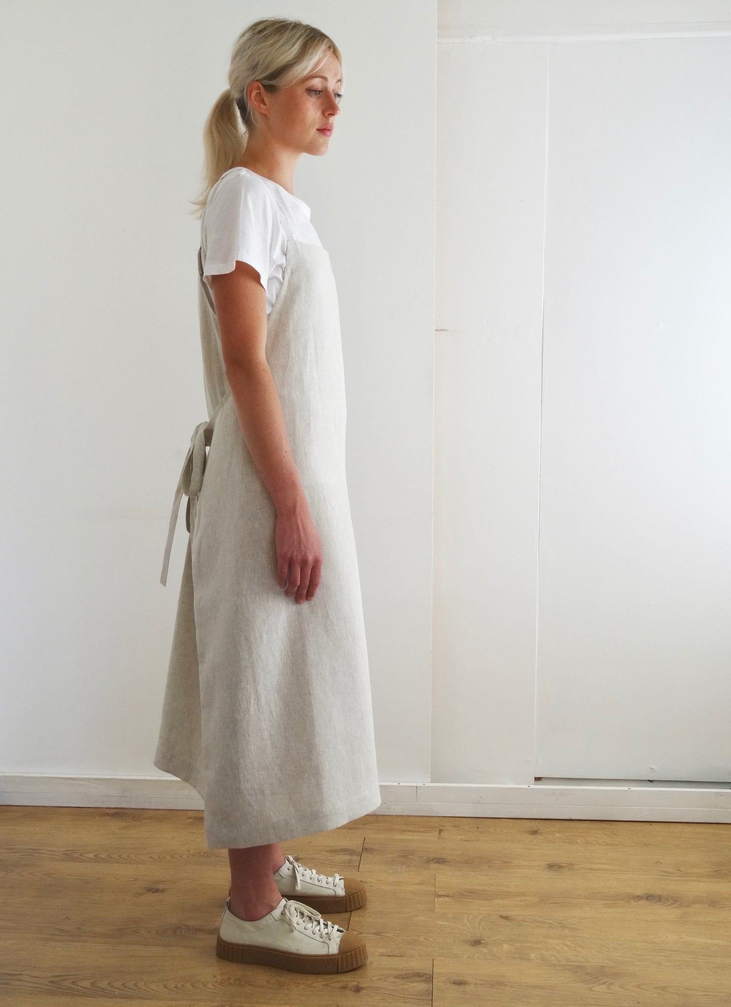 side view of young woman wearing a cream linen apron dress