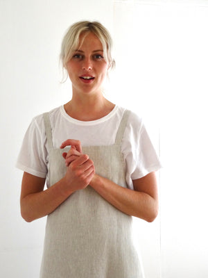 close up of young woman in bright room wearing a linen apron dress