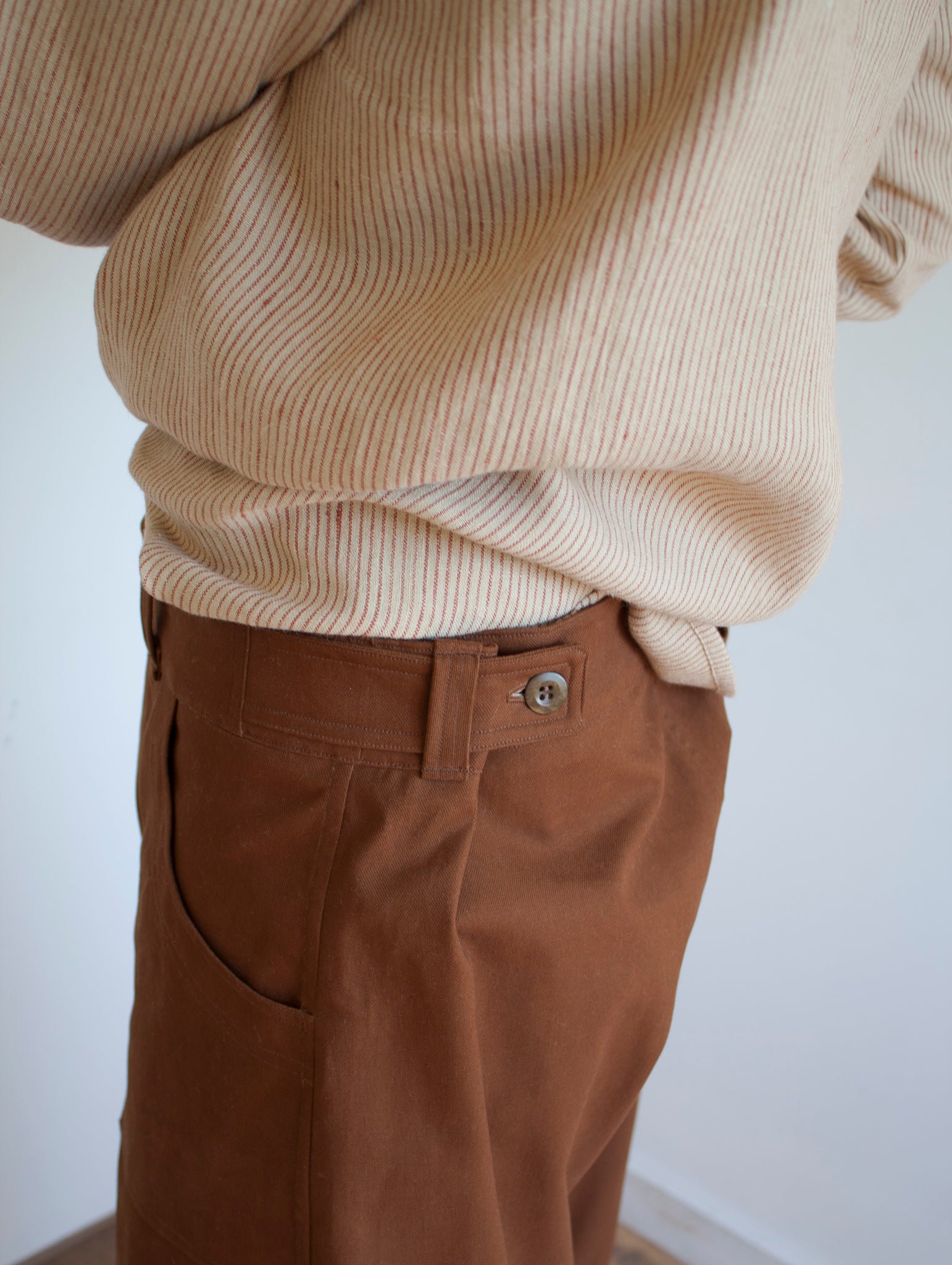 shop pajotten menswear close up image of the side view of a pair of chore trousers with side button fastening worn with a striped beige linen shirt