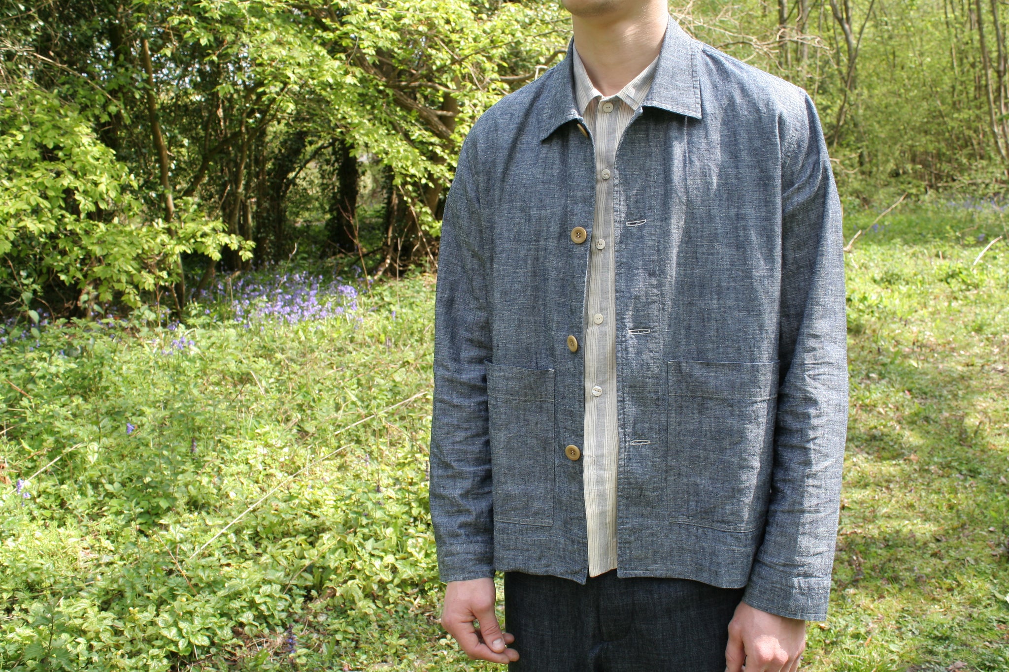 front detail of a denim jacket being worn by a young man standing in a springtime woodland setting