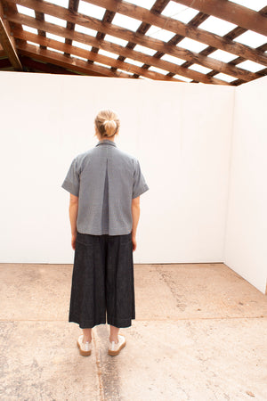 back view of a young white woman wearing a short sleeved gingham shirt and navy linen skirt