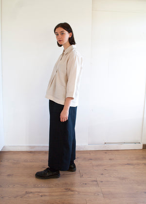 young pretty woman wearing a pair of navy linen trousers and a beige linen top standing in a white space