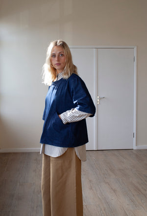 smiling blond woman standing in a sunlit room wearing an indigo denim overtop and skirt facing forward