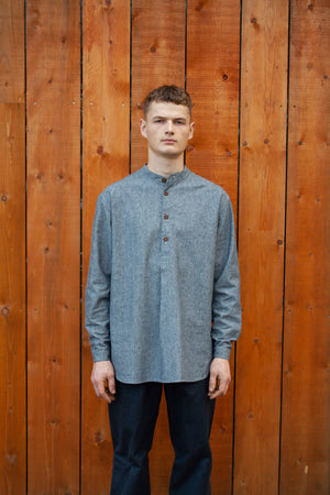 young man standing against a wooden wall wearing a blue cotton and hemp grandad shirt