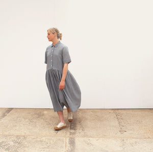 a woman walking in a white space wearing a gathered skirted gingham summer dress