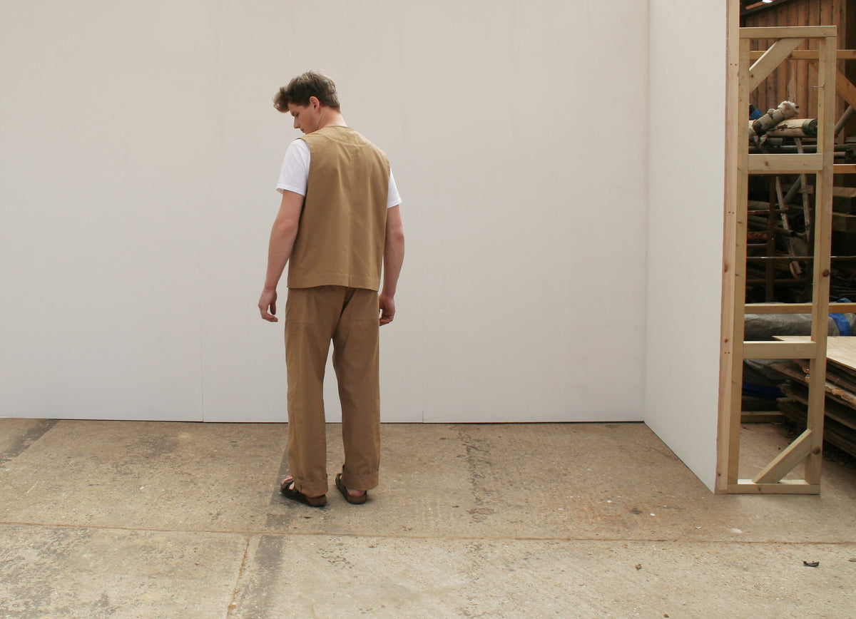 the back view of a man wearing a tan waistcoat and chore trousers
