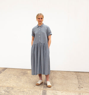 woman wearing as gathered waisted dress with her hands in the pockets