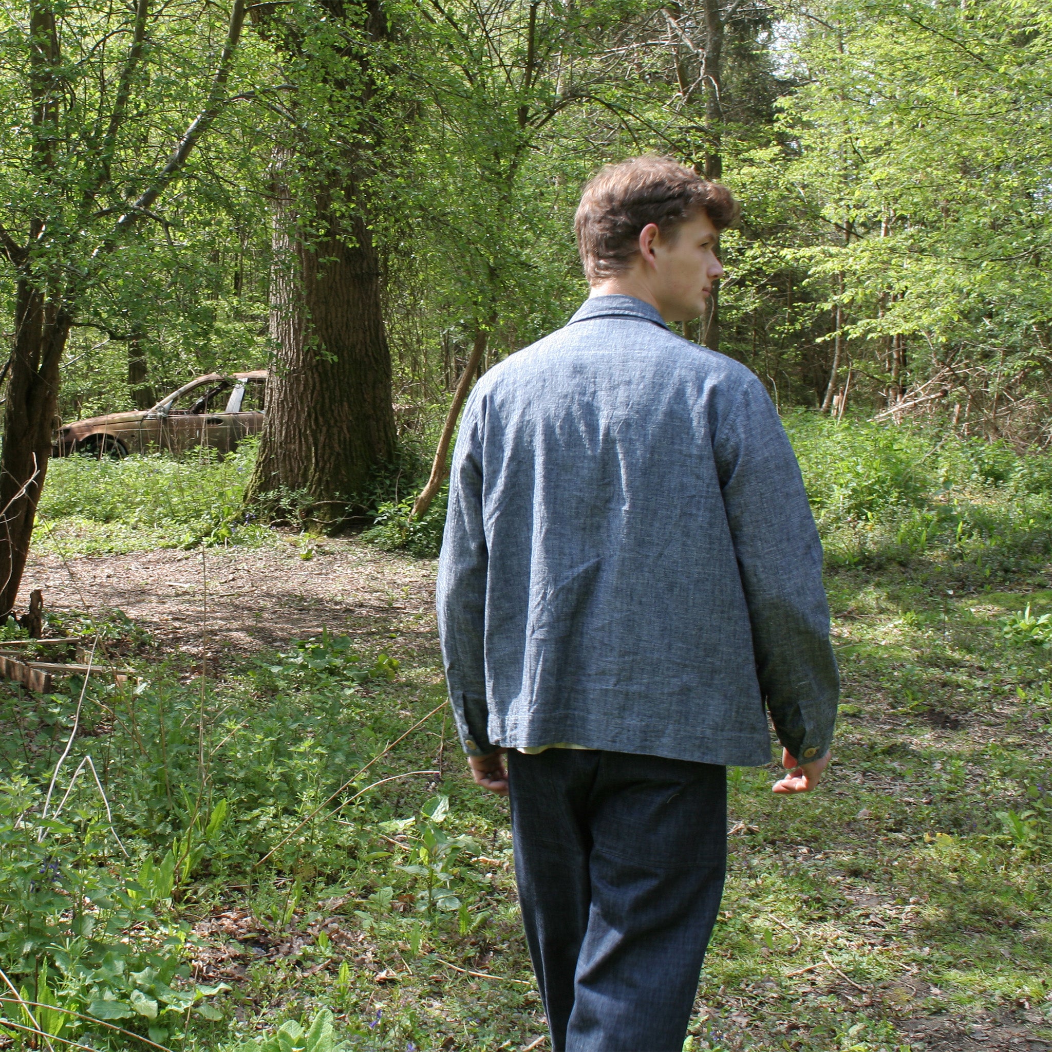 back view of a young man walking in a wood, wearing a denim chore jacket and jeans